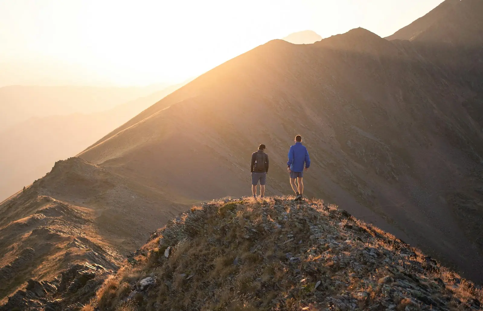 Two hikers walking a high mountain ridge into the golden light of sunrise